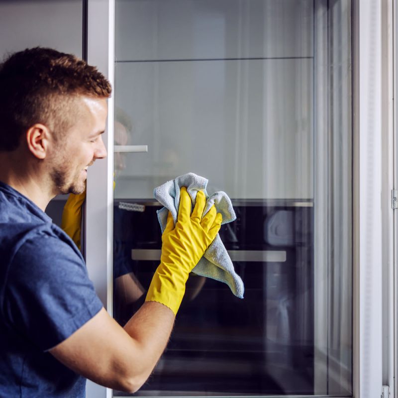 Reinigungskraft reinigt mit Lappen ein offenes Fenster.