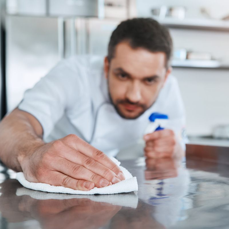 Küchenpersonal wischt mit Lappen über eine Arbeitsplatte.